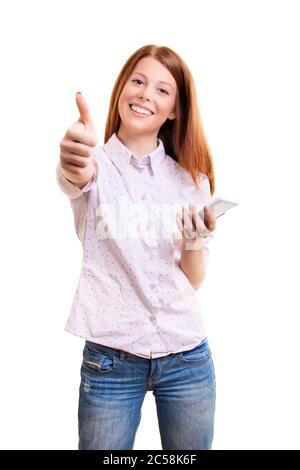 Portrait of a cheerful young girl in casual clothes holding mobile phone and giving thumb up, isolated on white background. Approval concept. Stock Photo