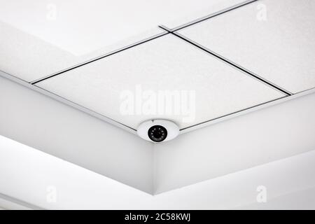 CCTV camera in the corner on a white suspended ceiling, security system close up. Stock Photo