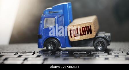 Toy truck moves wooden block with Follow word. depicts delivering goods or products around globe in e-Commerce. Business to Business concept. Logistic Stock Photo