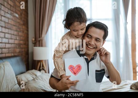 Asian little girl gives her father a heart-drawn paper as a symbol of love when meeting his father Stock Photo