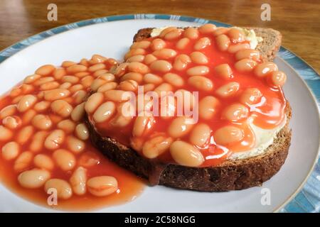 Close-up of freshly prepared, traditional Beans on Toast, in this case wholemeal bread. Ready to eat, the healthy snack can be seen on a wooden dinnin Stock Photo