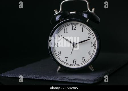 Black Alarm clock on a slate stone plate over black background. Selective Focus. Copy Space Concept. Mystery Stock Photo