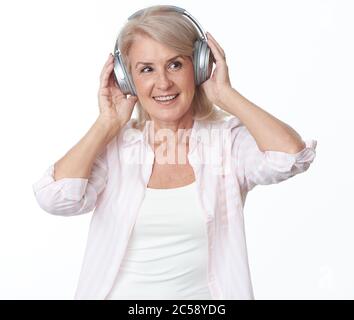 Cheerful 50 years old woman in headphones is listening to music. Isolated on white Stock Photo