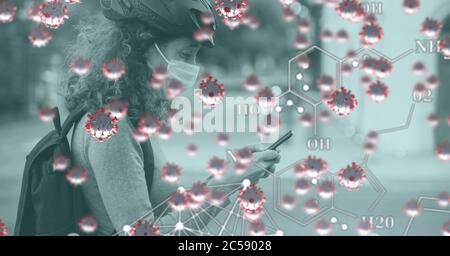 Covid-19 cells and chemical structures against woman wearing face mask using smartphone Stock Photo