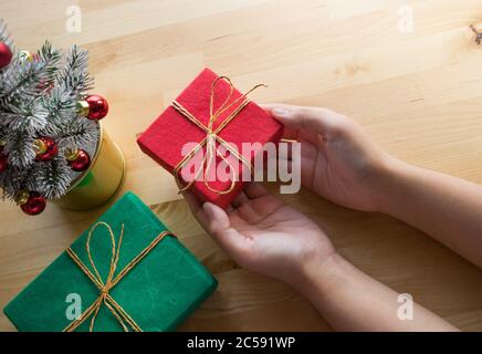 Merry christmas concepts with female hand holding gift box present and ornament element on wood table background.winter season's greeting ideas.top vi Stock Photo
