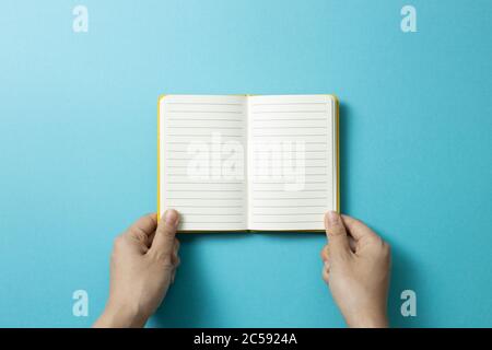 Hands open empty notebook on blue background. top view, copy space Stock Photo