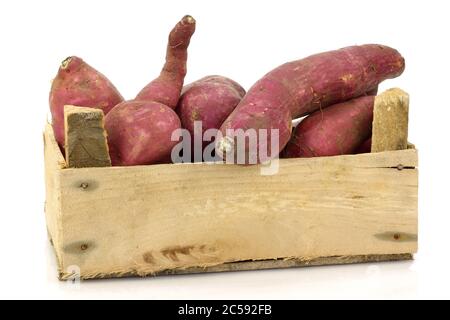 Bunch of sweet potatoes and a cut one in a wooden crate on a white background Stock Photo