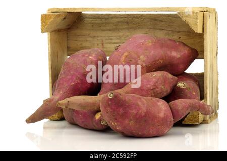 Bunch of sweet potatoes and a cut one in a wooden crate on a white background Stock Photo