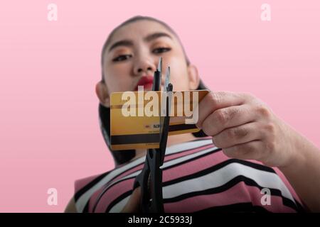 Portrait of young Asian woman cutting up a credit card with scissors to stop spending on shopping at the pink background Stock Photo
