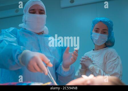 close-up in focus of the hands of pediatric surgeons in gloves, perform an operation on a small patient, the stage of processing the surgical field Stock Photo