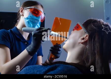 Portrait of a dentist doctor performing the procedure of professional teeth whitening using ultraviolet radiation. Patient and doctor in protective Stock Photo