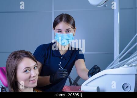 a dentist in a mask and gloves, shows a happy patient an x-ray of the teeth, telling her about the pathology of the tooth. In the dental office Stock Photo