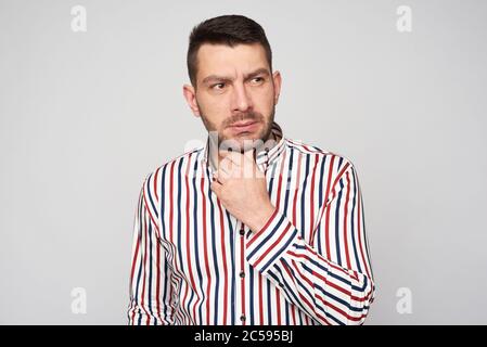 thoughtful bearded man is wearing striped shirt looking away isolated on grey studio wall Stock Photo