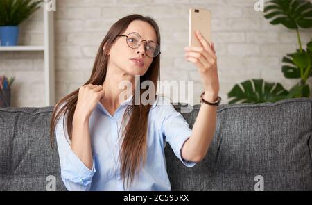 Brunette woman is taking selfie on her smartphone while sitting on a couch at home Stock Photo