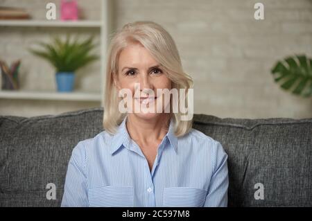 Lovely middle aged blond woman with a beaming smile sitting on a sofa at home Stock Photo