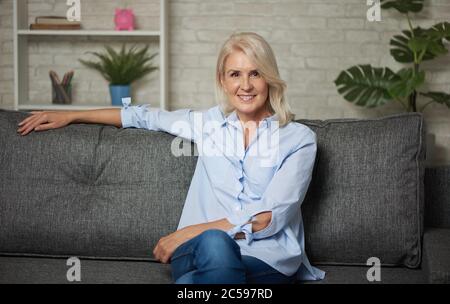 Pretty middle aged woman is sitting on a sofa at home Stock Photo