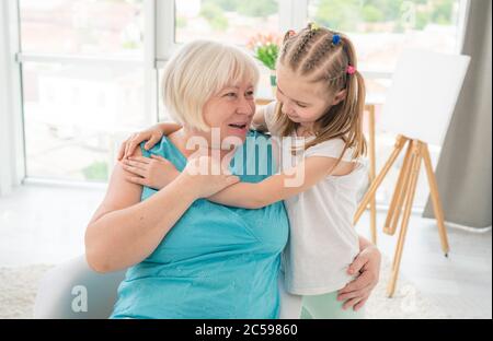 Cute little girl embracing smiling granny in light room Stock Photo