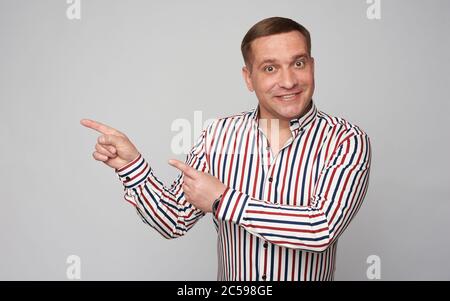Middle aged man is pointing his finger at copy space. Isolated on grey Stock Photo