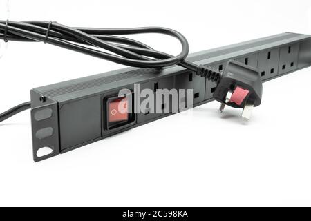 Isolated view of a 19-inch, rack mount power distribution socket showing its UK plug, sockets and illuminated on and off switch. Stock Photo
