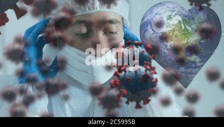Covid-19 cells and heart shaped globe against doctor wearing face mask Stock Photo