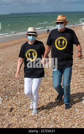 Southsea, Portsmouth, England, UK. 2020. Elderly couple walking on the beach wearing masks and, keep your distance shirts during Covid-19 lockdown. Stock Photo