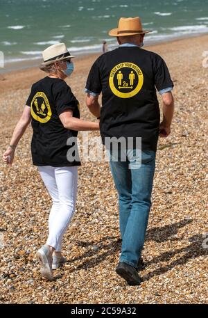 Southsea, Portsmouth, England, UK. 2020. Elderly couple walking on the beach wearing masks and, keep your distance shirts during Covid-19 lockdown. Stock Photo