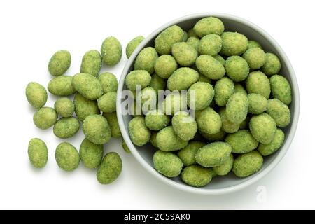Wasabi coated peanuts in a white ceramic bowl next to a pile of wasabi peanuts isolated on white. Top view. Stock Photo