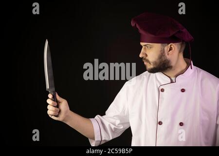 Young handsome bearded chef man in uniform holds knife in hand stares intently Stock Photo