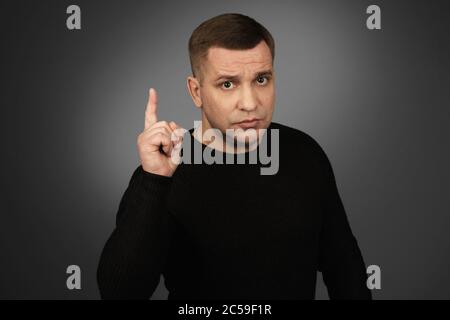 man in black sweater pointing his finger up. Studio shot Stock Photo