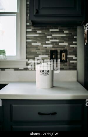 A white jar of ground coffee sits on white countertop in a kitchen. Stock Photo