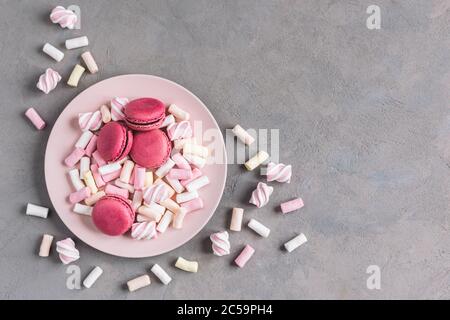 Tasty pink french macaroons and marshmallows on a plate. Grey background. Place for text. Stock Photo