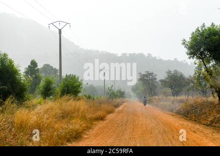 Africa, West Africa, Benin, Natitinqou. A man on a scooter walks along a dirt road in northern Benin. Stock Photo