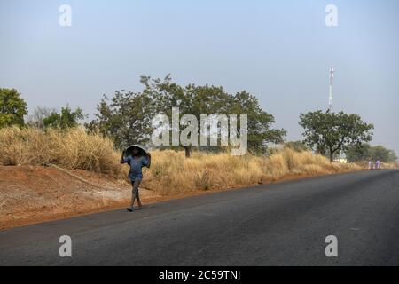 Africa, West Africa, Benin, Natitinqou. A young boy walks with an overturned bucket on his head on a road in northern Benin. Stock Photo