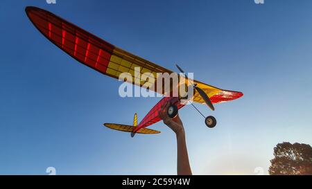 Low angle shot of a male hand holding an old radio controlled guard plane on blue sky background Stock Photo