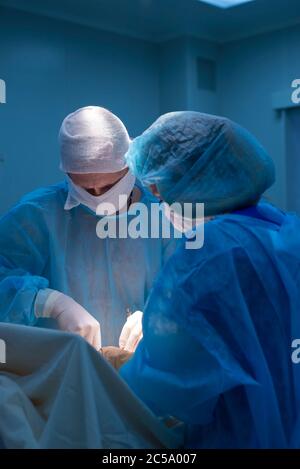 Children's surgeons perform urological surgery. A man and a woman in a mask, and a blue sterile gown, in the operating room. Stock Photo