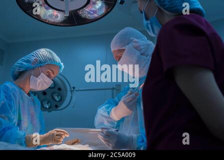 Children's surgeons perform urological surgery. A man and a woman in a mask, and a blue sterile gown, in the operating room. bottom view Stock Photo