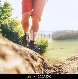 Close up image backpacker traveler feet in trekking boots on mountain dirty path at summertime sunny day. Stock Photo