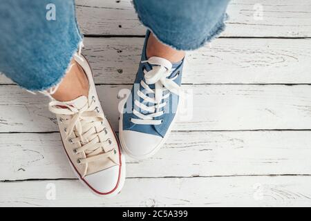 Teenager's feet in different colors beige and blue casual new sneakers on the white wooden floor close up image. Vintage style in modern fashion world Stock Photo