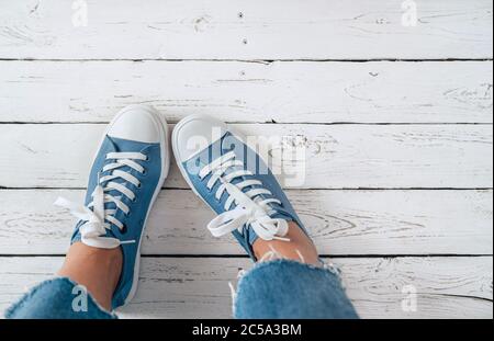 Teenager's feet in blue color casual new sneakers with white shoelaces on the white wooden floor close up image. Vintage style in modern fashion world Stock Photo