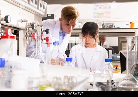 Young Caucasian and Asian students engaged in research at chemical lab Stock Photo