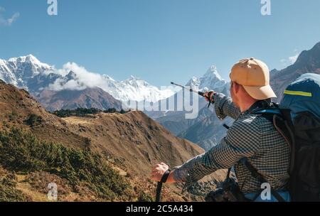 Hiker backpacker man using trekking poles pointing to Everest 8848m mountain during high altitude Acclimatization walk. Everest Base Camp trekking rou Stock Photo