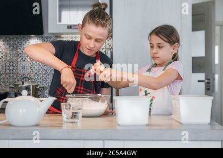 Kids Home cooking concept image. Sister and Brother dressed aprons making a homemade pancakes on the home kitchen. Boy mixing a liquid dough and girl Stock Photo