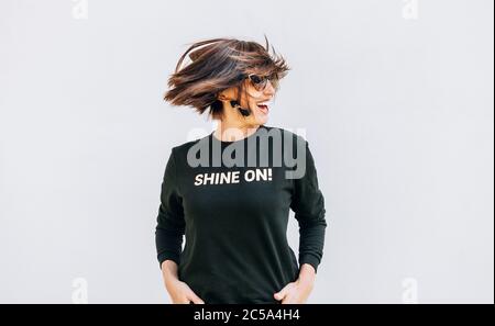 Free feeling happy smiling woman posing in black sweatshirt with positive print Shine On. She rotating a head bacause a cheerful mood. Stock Photo