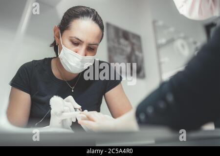 Professional manicure master dressed black in safety face mask using Electric Nail Polisher Tool for Glazing treatment manicure procedure. Small busin Stock Photo