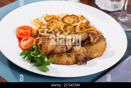 Roasted rabbit liver served with fried onion, fresh tomato and greens on white dish Stock Photo