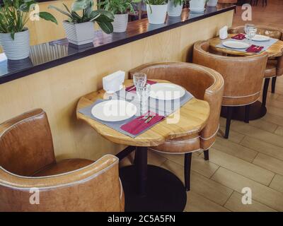 Two small tables with wooden countertops and armchairs near them stand at a high shelf with plants in pots Stock Photo