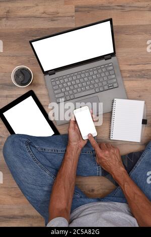 High angle of a male sitting on the floor with his Electronic Devices - Smartphone, Laptop Computer and Tablet with blank white screens ready for your Stock Photo