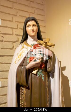 Interior scene woman saint sculpture holding a cross over brickwall background Stock Photo