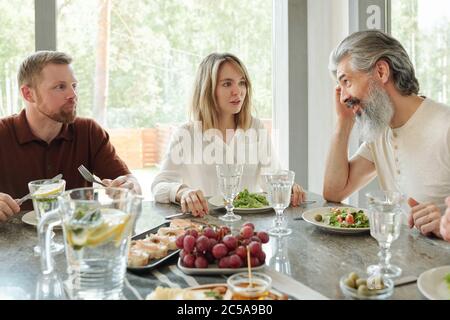 Senior father with gray beard sitting at table and talking to daughter and her husband during dinner Stock Photo