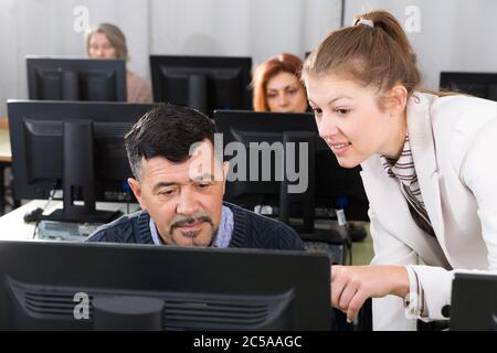 Portrait of middle aged man attentively listening young female coach during computer classes at university of third age Stock Photo